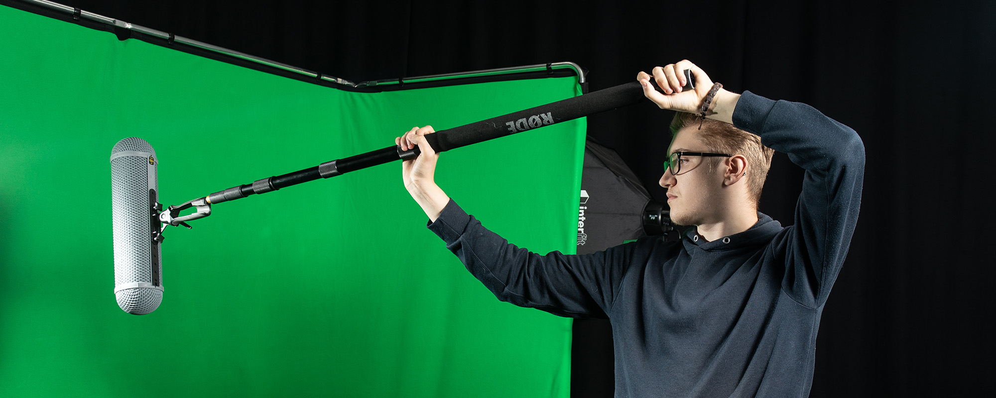 A student holding a boom microphone in front of a green screen