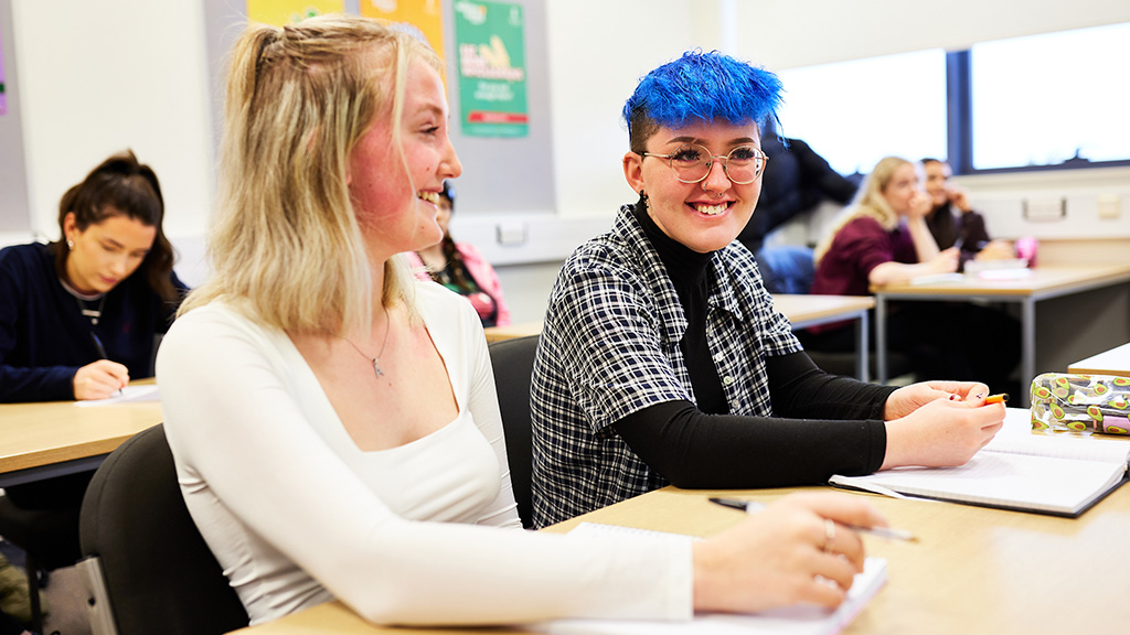 Two female students in class smiling