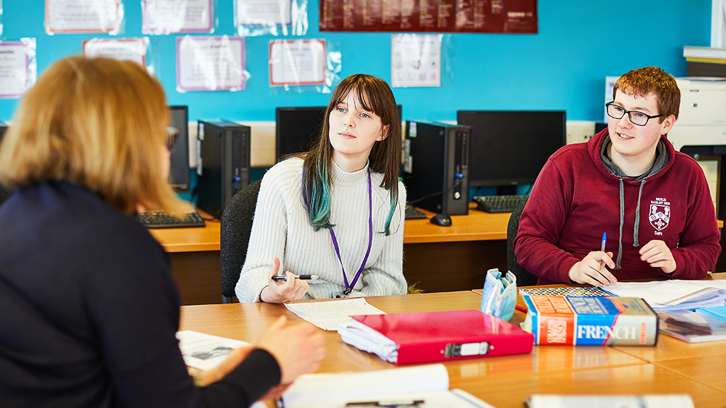 Two students talking to their tutor in class