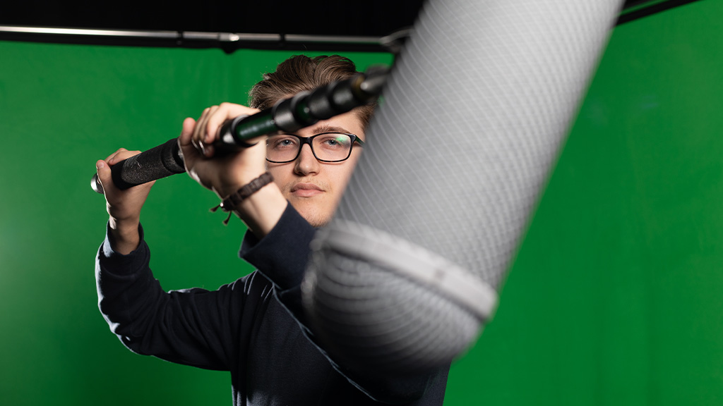 Student holding a mic boom against a green screen